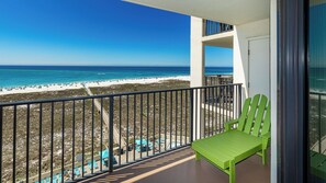 A balcony with a green chair, a view of a beach, and a clear blue sky.