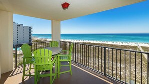 A balcony with a table and chairs, overlooking a beach and ocean.