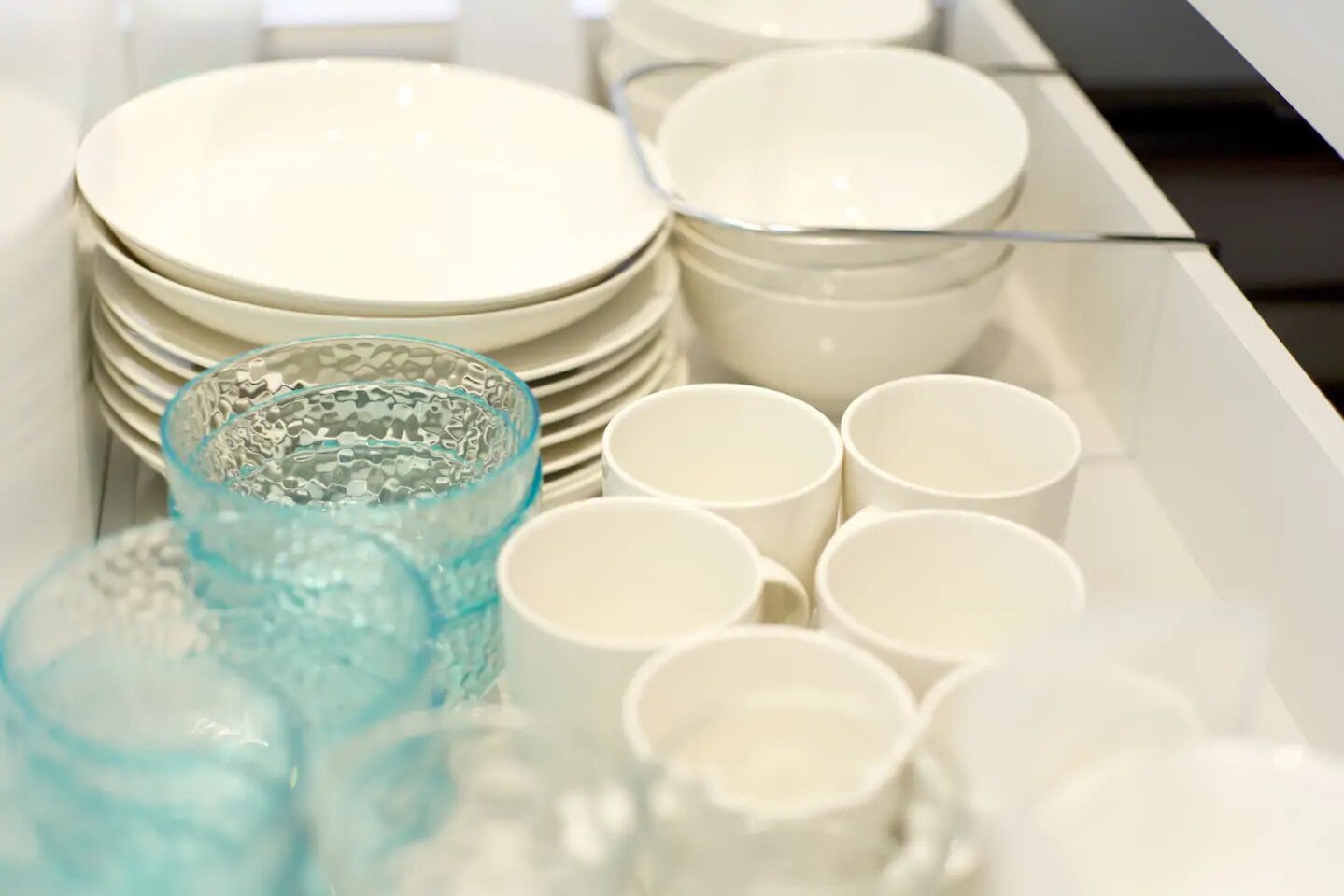 A neatly organized drawer with stacks of white plates, bowls, and a blue glass.