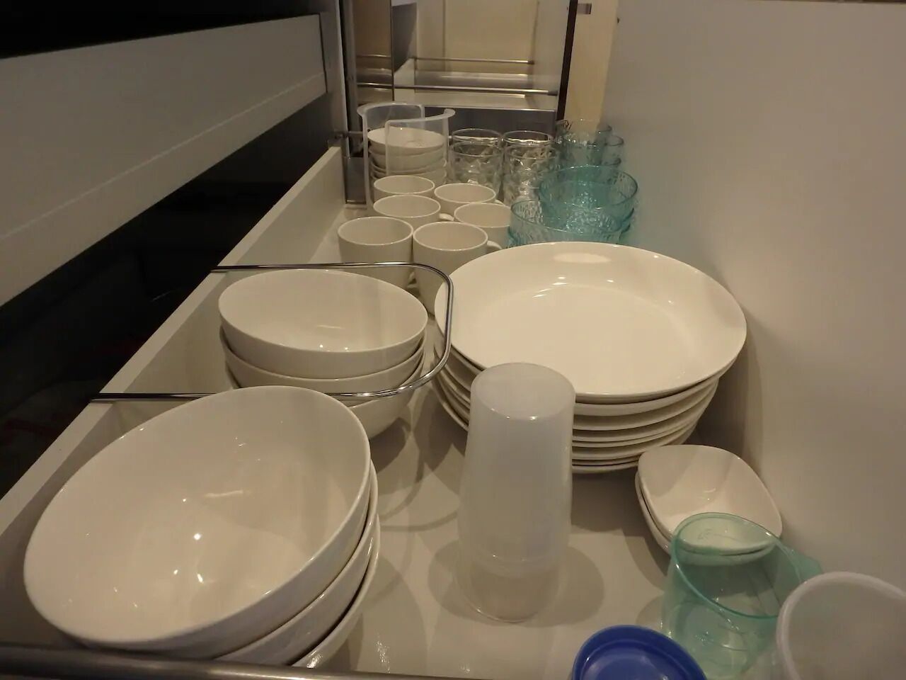 A kitchen area with various white dishes and glassware, including bowls, plates, and cups, neatly arranged on a counter.