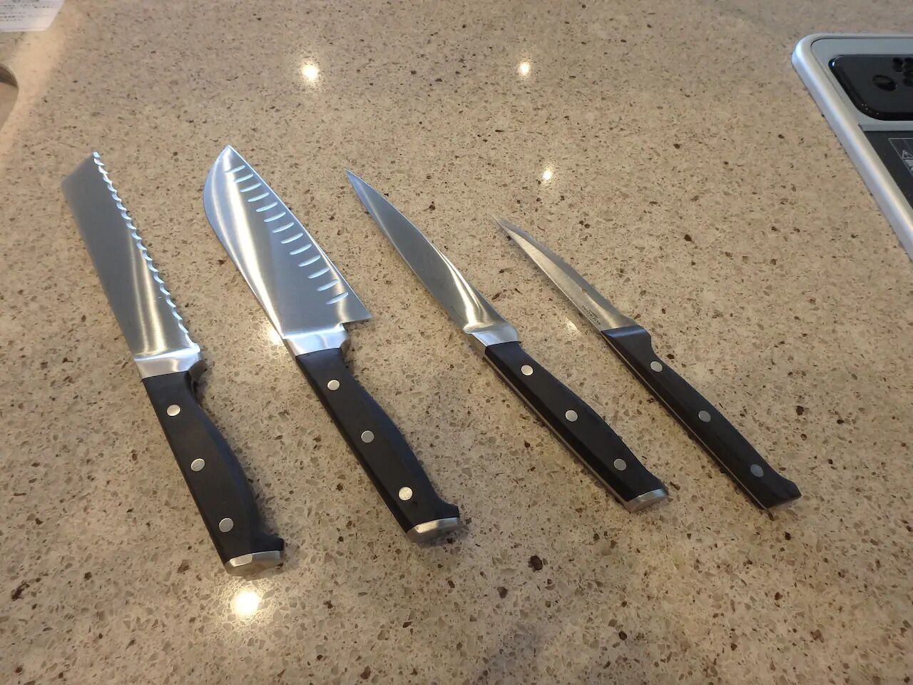 Vier Küchenmesser mit schwarzen Griffen und metallischen Klingen auf einer fleckigen Arbeitsplatte.
