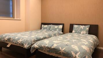 Two twin beds with matching blue bedding featuring sea creatures, positioned against a wooden wall with a window above.