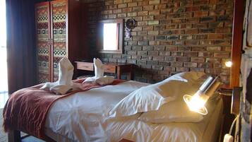 Habitación de hotel con pared de ladrillo, cama con ropa blanca, manta roja y ventana con luz natural.
