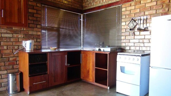 A compact kitchen with wooden cabinets, a white stove, and a window with blinds.