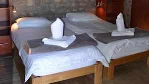 A room with a stone wall, wooden bed frames, and a thatched roof. - West Nest Lodge (Witvlei)