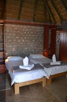 Um quarto com parede de pedra, estruturas de cama de madeira e telhado de palha.