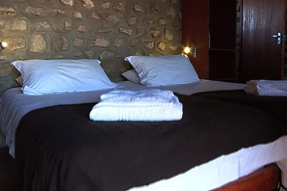 A room with a stone wall, a wooden door, and two beds with white linens and towels.