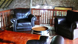 A rustic interior with leather sofas, a wooden barrel, and a brick wall. - West Nest Lodge (Witvlei)
