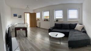 Een moderne woonkamer met een hoekbank, een eettafel met stoelen en een flatscreen televisie.