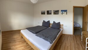 Een slaapkamer met een houten bed, een klein nachtkastje en een houten plank.