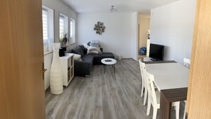Een moderne woonkamer met een bank, een salontafel en een televisie. Er is een eethoek met een tafel en stoelen.