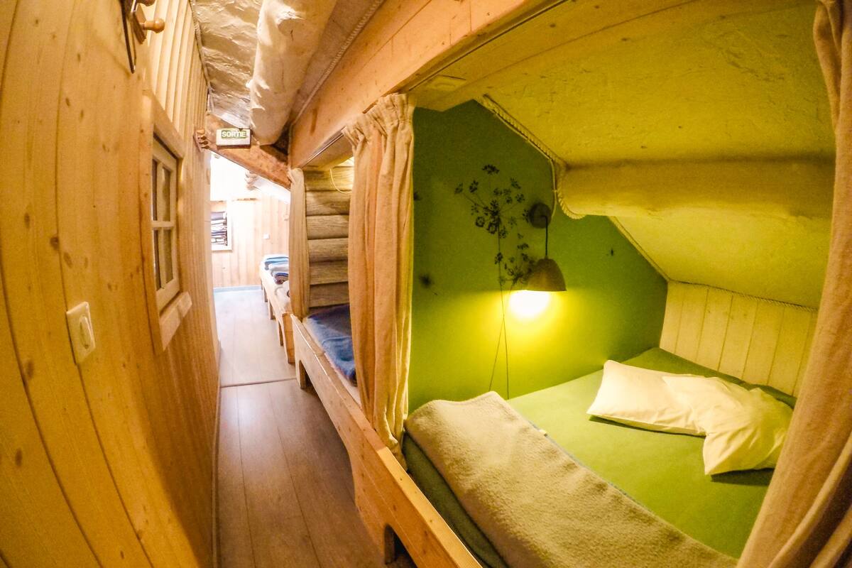 Ein schmaler Korridor mit Holzwänden und einem Bett mit grünen Wänden sowie einer hängenden Lampe.