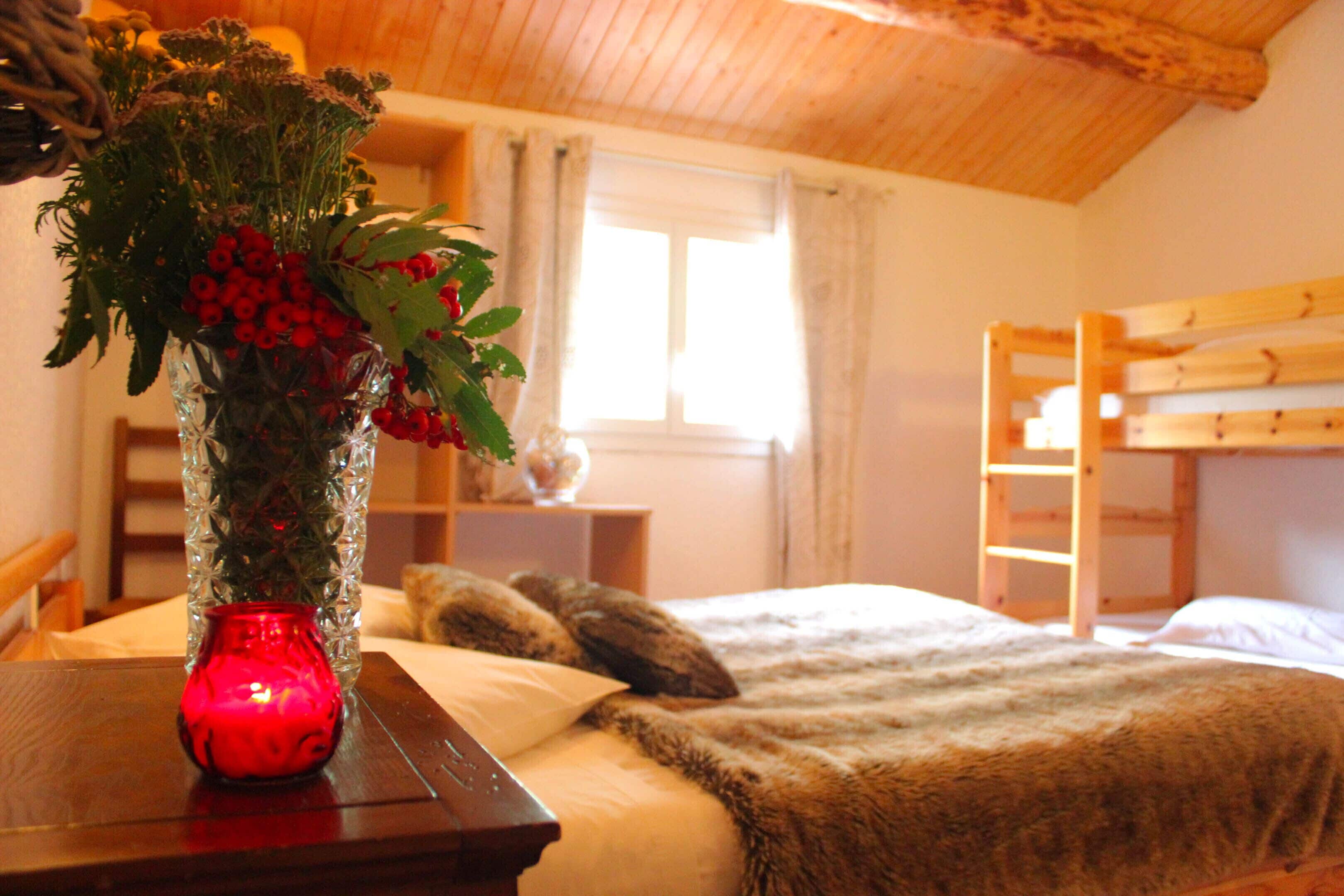 A cozy room with a wooden bunk bed, a wooden table with a red vase, and a window with curtains.