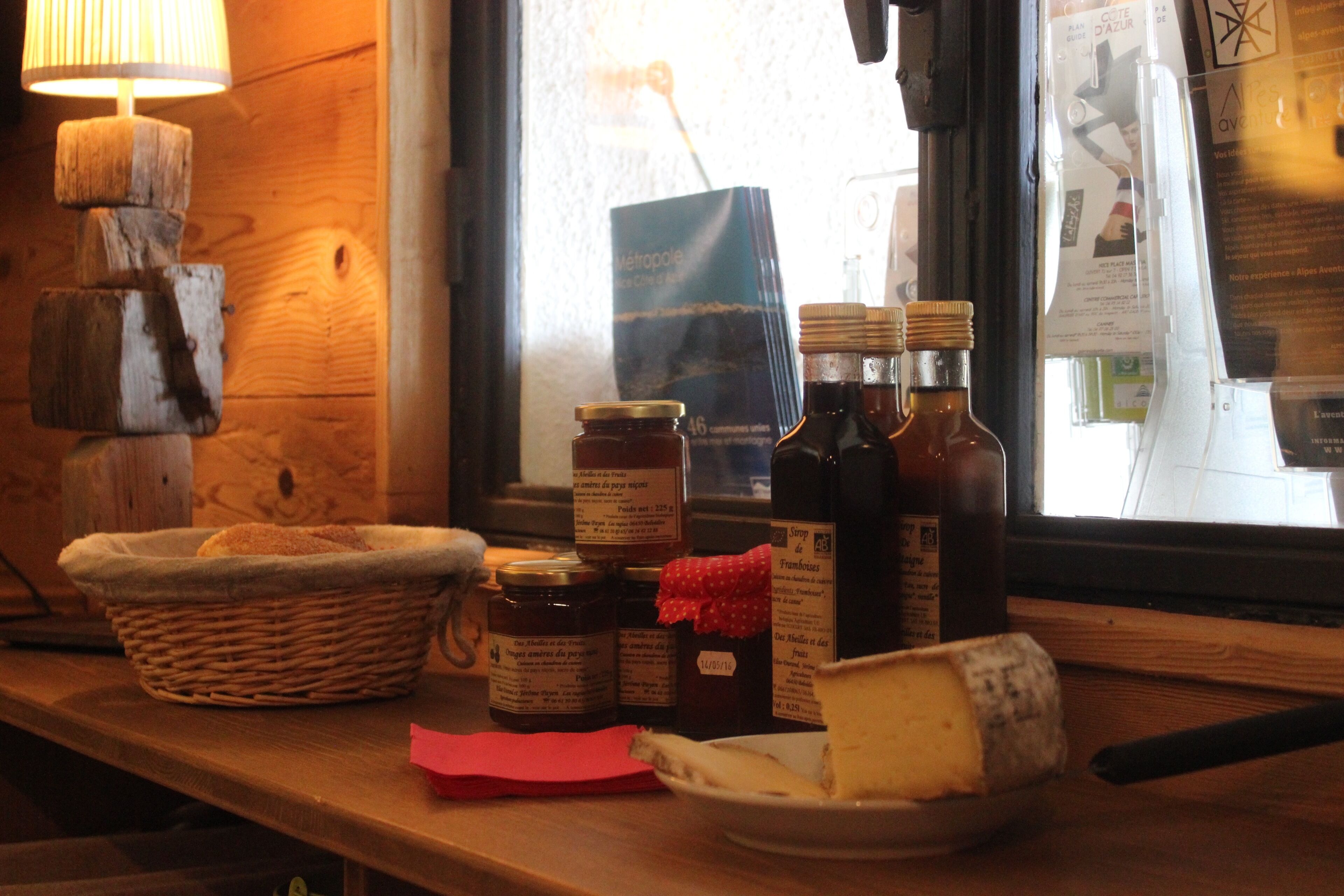 A wooden table with a basket of bread, jars of preserves, and bottles of liquid.