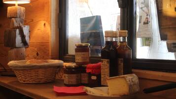A wooden table with a basket of bread, jars of preserves, and bottles of liquid.