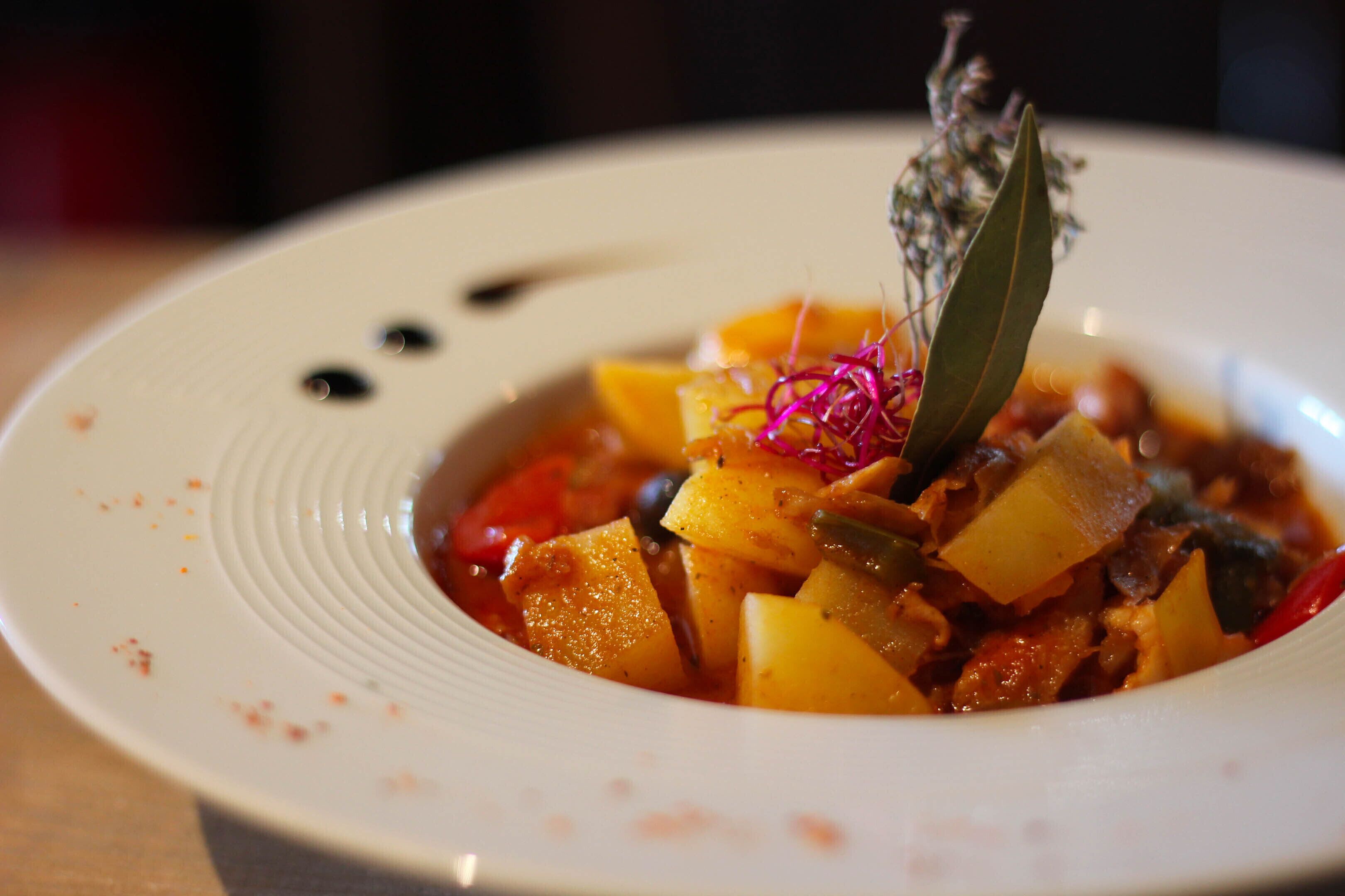 Une assiette blanche contenant un plat de légumes colorés, agrémenté d’une branche d’herbe aromatique.
