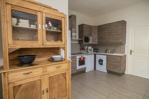 A kitchen with wooden cabinets, a microwave, a washing machine, and a sink. - Domaine Castell de Blés - Gîte Vermeille (Saint-Genis-des-Fontaines)