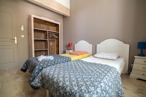 A bedroom with two beds, a wooden wardrobe, a nightstand, and a desk with a lamp. - Domaine Castell de Blés - Gîte Vermeille (Saint-Genis-des-Fontaines)