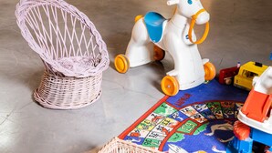 Una habitación con una mesa de comedor, sillas, una silla de mimbre, un caballo de juguete y una colchoneta para jugar.