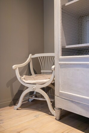 A white chair with a cushion against a wall, next to a white cabinet with a mesh screen. - Domaine Castell de Blés - Gîte Vermeille (Saint-Genis-des-Fontaines)