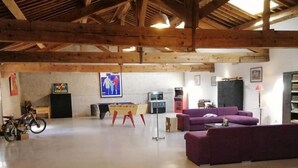 Amplia habitación con techo de madera, un sofá morado, una mesita y una bicicleta.
