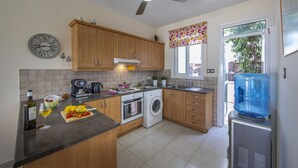A kitchen with wooden cabinets, a washing machine, a coffee maker, and a water dispenser. - Protaras Villa Marilia Near Fig Tree Bay Beach (Protaras)