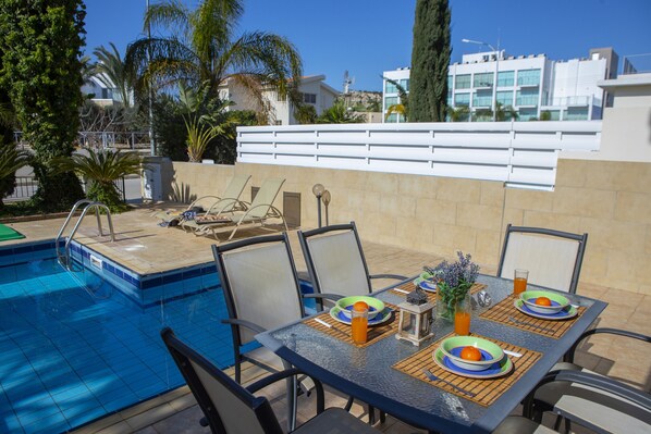 Un espace extérieur aménagé pour les repas, avec une piscine, des chaises et des tables pour deux personnes.