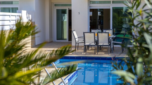 A modern outdoor pool area with a table and chairs, surrounded by glass doors and a number '5' sign. - Protaras Villa Marilia Near Fig Tree Bay Beach (Protaras)