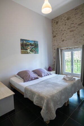 Een slaapkamer met een bed, een schilderij, een raam met gordijnen en een klein tafeltje.
