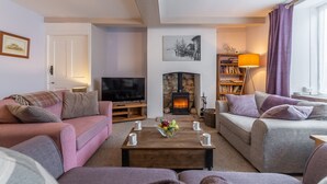 Ein gemütliches Wohnzimmer mit Kamin, Sofas, einem Couchtisch mit Obstschale und einem Bücherregal.