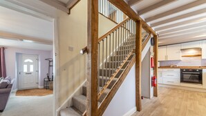 Eine Treppe mit Holzgeländern führt zu einer zweiten Etage. Rechts ist eine Küche mit weißen Schränken und einem Herd zu sehen.