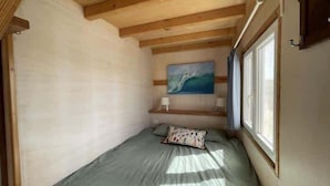 Una stanza piccola e stretta con un letto, un quadro appeso al muro e una finestra.