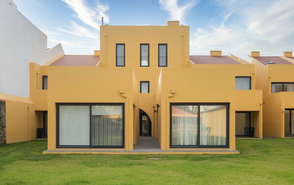 Un bâtiment moderne à la façade jaune, doté de grandes fenêtres et d’une entrée centrale.