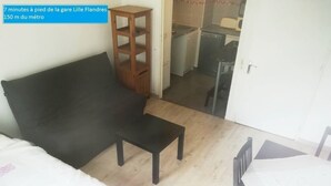 A small room with a bed, a wooden stool, a table, and a kitchenette in the background. - LUMINOUS Apartment (strasbourg)