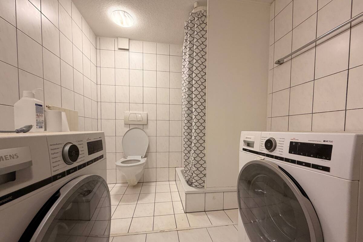 Une petite salle de bain comprenant des toilettes, une douche avec un rideau à motifs et deux machines à laver à chargement frontal.