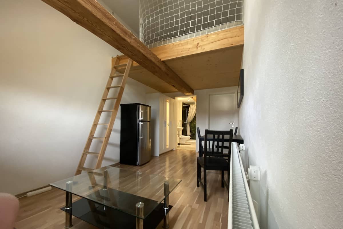 Une cuisine moderne avec une table à plateau en verre, un réfrigérateur et un escabeau en bois.