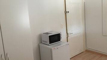 Una cocina compacta con un microondas sobre un refrigerador pequeño, una puerta blanca y piso de madera.