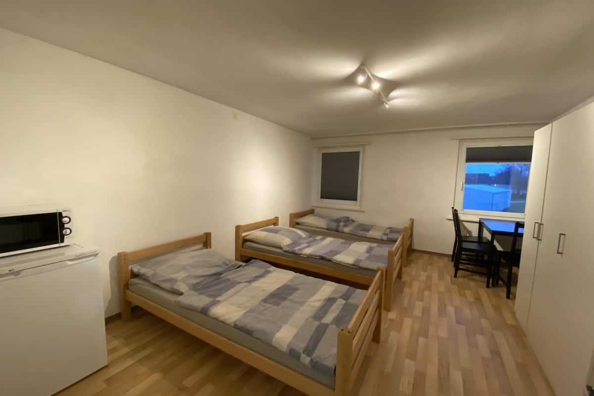 Une petite pièce compacte comprenant deux lits en bois, une petite kitchenette, une fenêtre et un bureau avec une chaise.