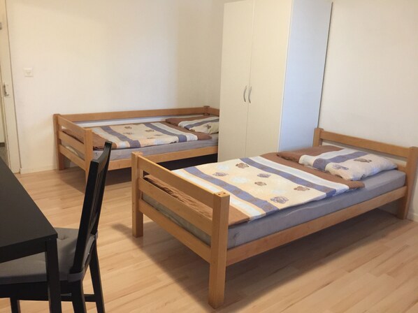 A room with two wooden bunk beds, a desk with a chair, and a wardrobe. - Hostel Airport Oberglatt (Oberglatt)