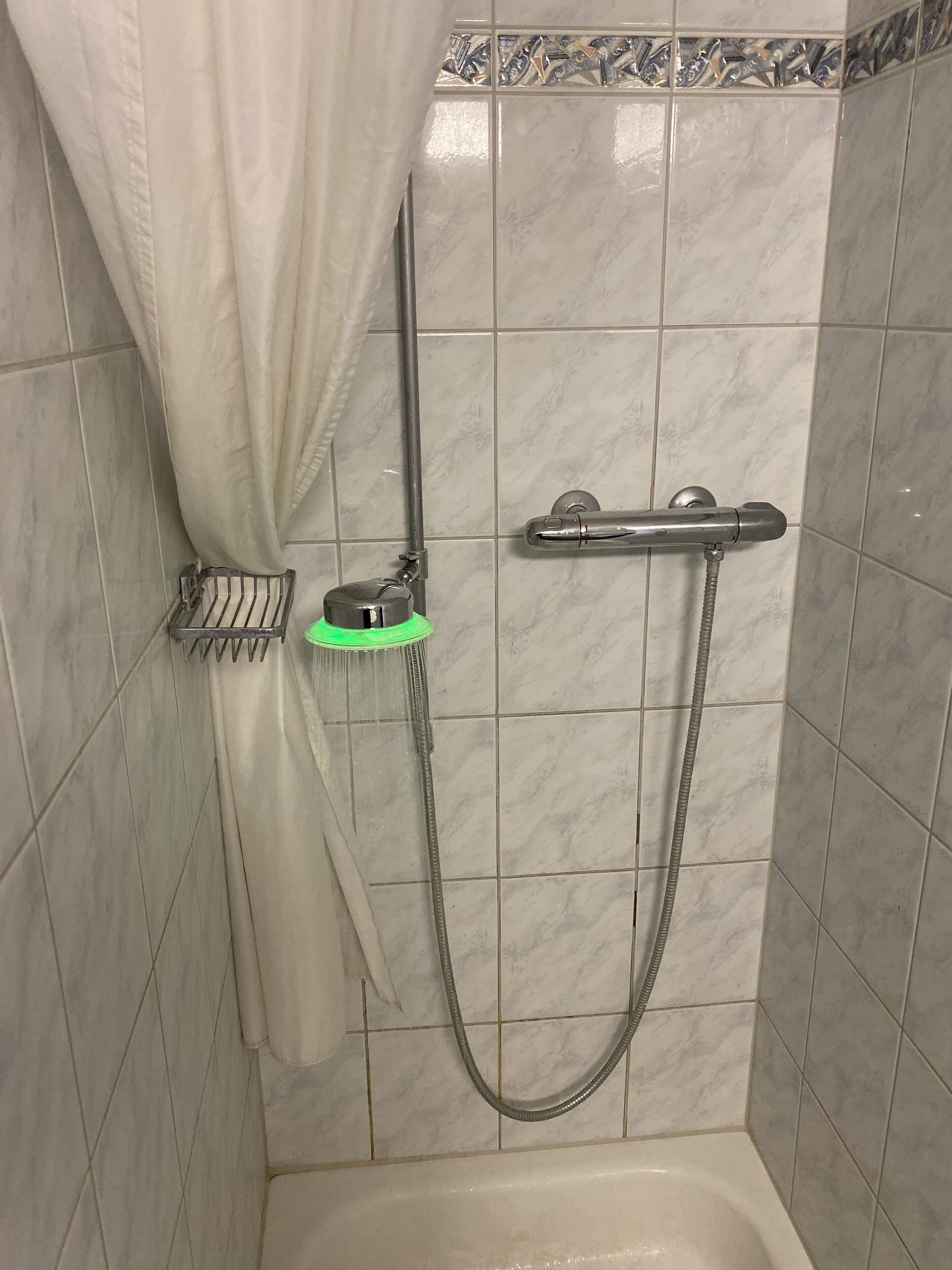 Un área de ducha con cabezal de ducha de mano, grifo empotrado y cortina de ducha.