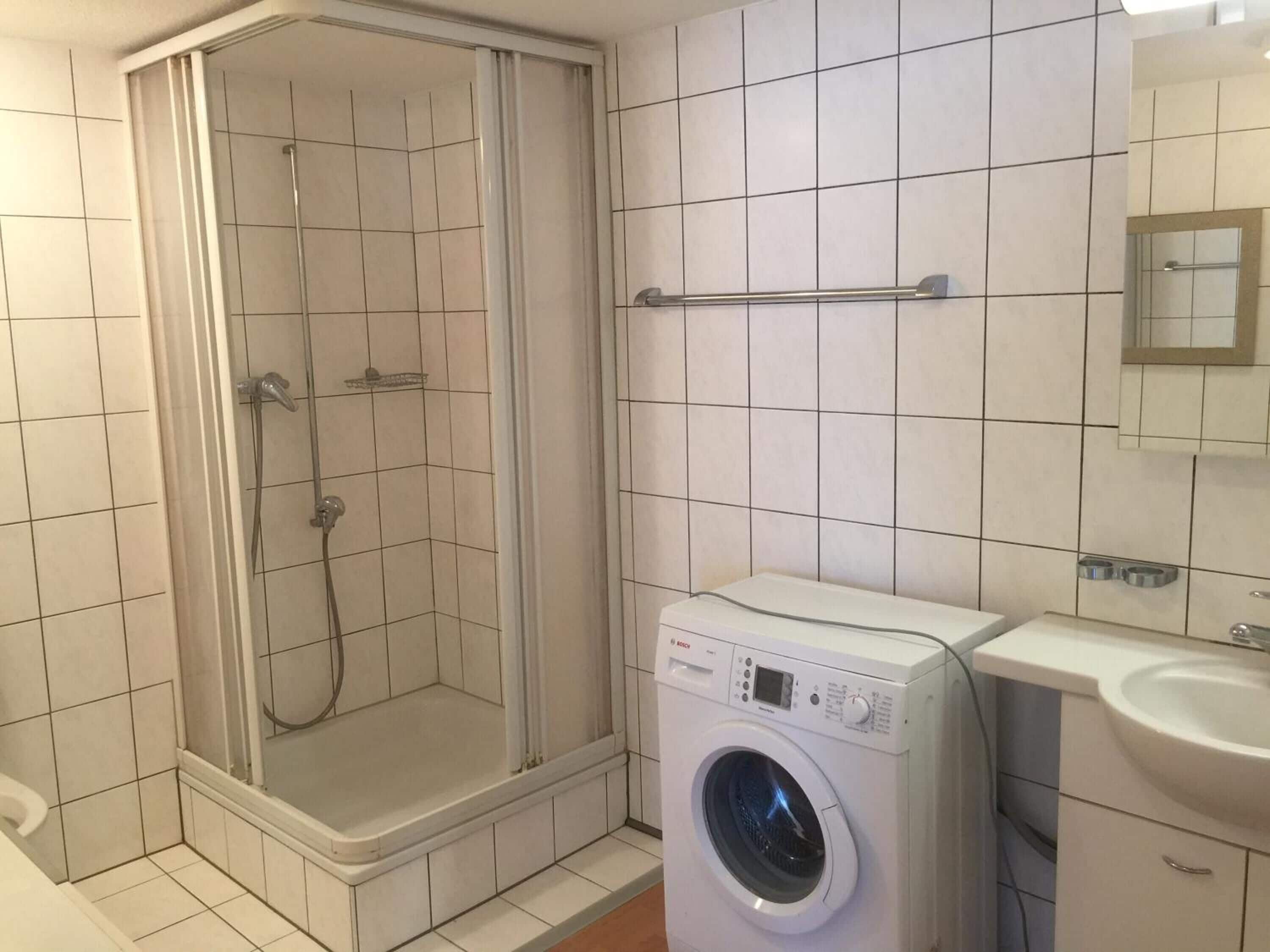 Ein Badezimmer mit Dusche, Waschmaschine und Waschbecken.