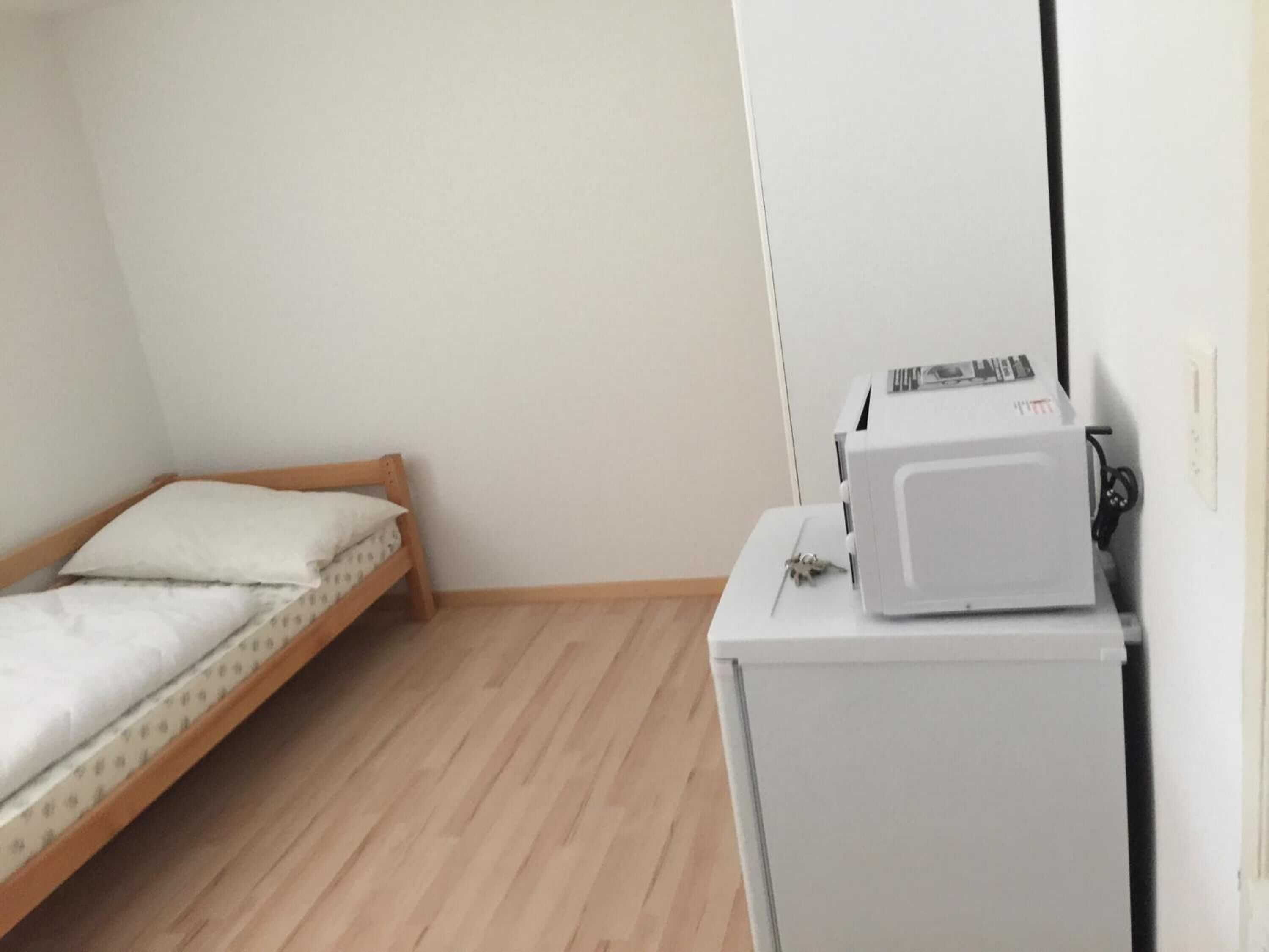 Una habitación pequeña con una cama de madera y un refrigerador blanco.