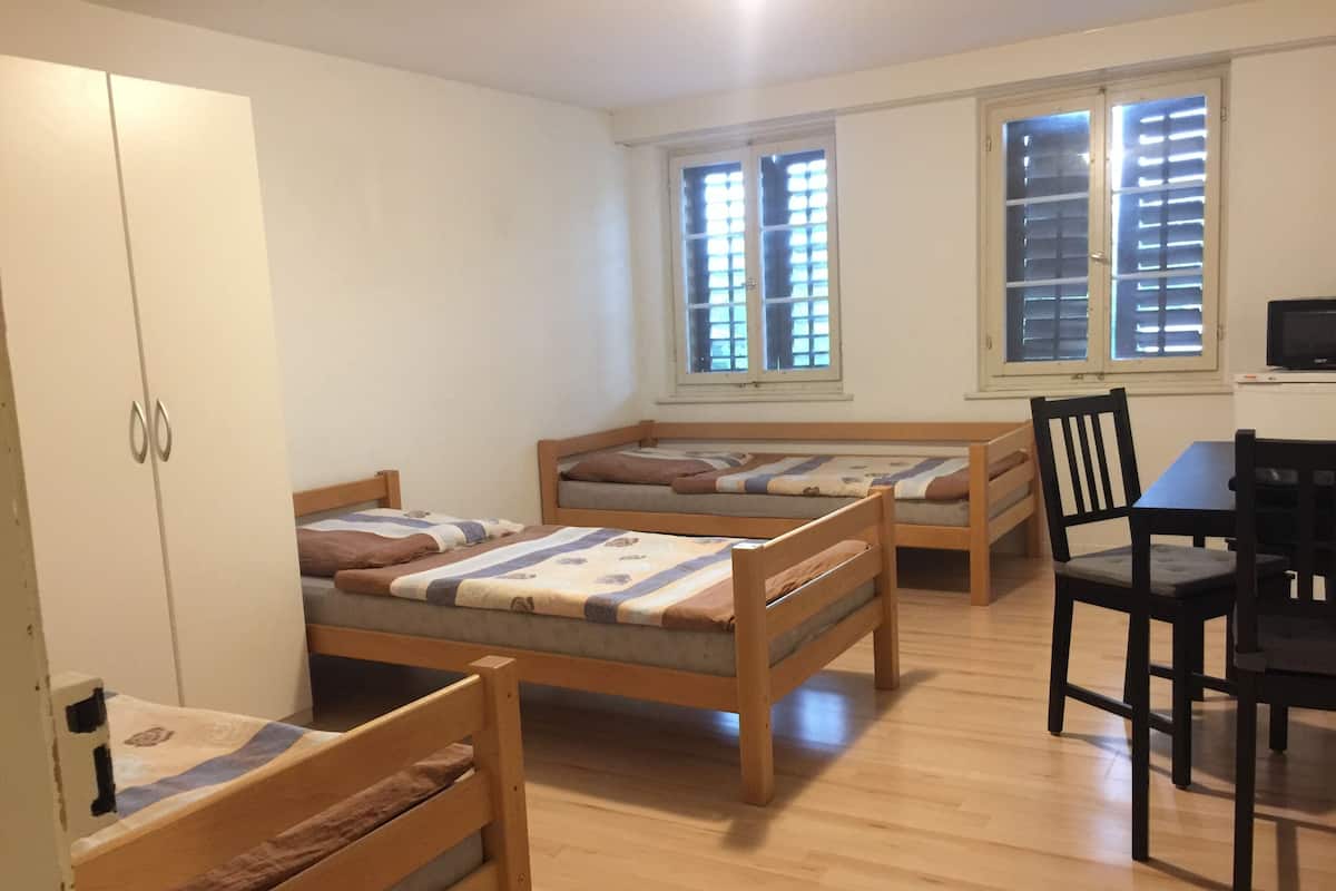 Une chambre avec deux lits simples, une armoire en bois, une table à manger avec des chaises et un téléviseur.