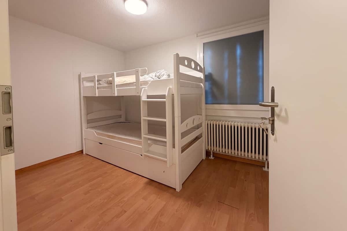 Une chambre avec un lit superposé, un radiateur et une fenêtre avec des rideaux.