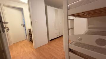 A bedroom with a bunk bed, wooden flooring, white walls, and a door leading to another room.