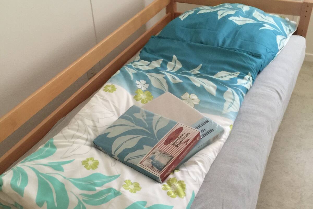 Un lit simple avec un cadre en bois, une couvre-lit à motifs floraux et un oreiller bleu.