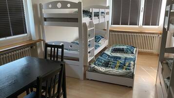 Ein Kinderstockbett mit Schreibtisch, Stuhl, Heizkörper und jalousieförmigen Vorhängen an den Fenstern.