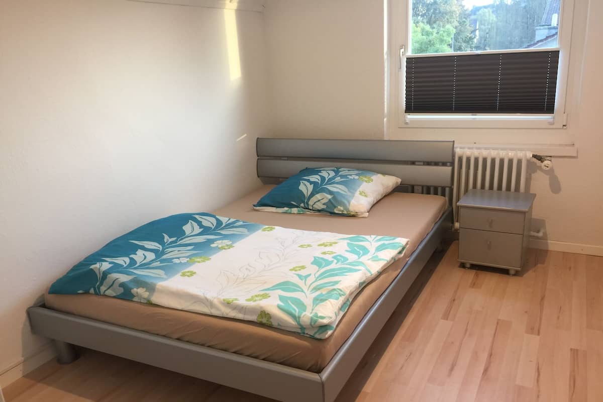 Une chambre à coucher avec un lit, une table de chevet et une fenêtre avec des stores.