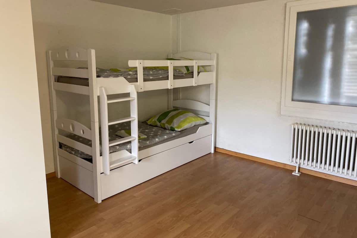 Un lit superposé avec des tiroirs de rangement, une fenêtre avec des stores et un radiateur.