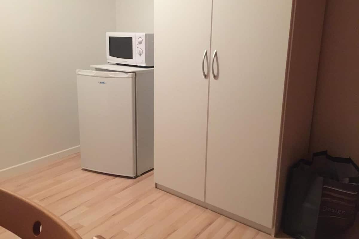 Une petite pièce avec un réfrigérateur blanc, un four à micro-ondes posé sur le dessus, et une armoire à deux portes.